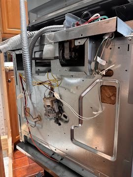 Rear service panel removed from an oven showing plumbing and wiring